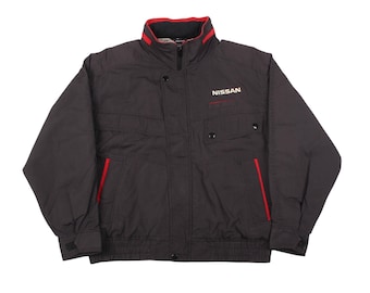 May include: A black jacket with red accents, featuring a stand-up collar and a zipper closure. The jacket has two front pockets and the word "NISSAN" printed on the chest. The jacket's design includes red piping along the pockets and collar.