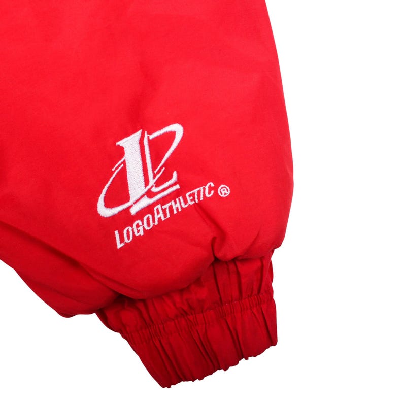 May include: A bright red jacket sleeve featuring an elasticized cuff. The fabric displays white embroidered text that reads LOGOATHLETIC along with a stylized letter L logo positioned above the brand name on the outer side of the sleeve.