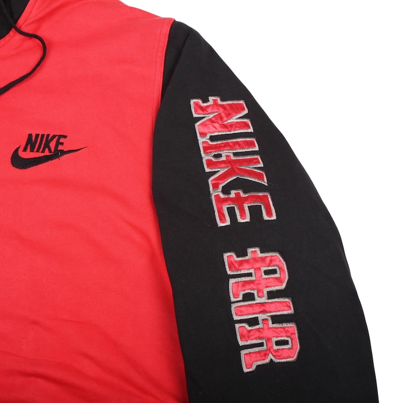 Pu&ograve; includere: Felpa con cappuccio Nike rossa e nera. La felpa ha un corpo rosso e maniche nere. Il logo Nike &egrave; ricamato in nero sul petto. La manica destra presenta la scritta "NIKE AIR" ricamata in rosso.