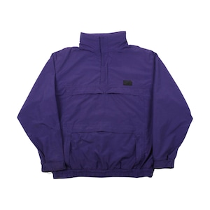 Op de afbeelding: Een paarse anorakjas met een hoge kraag en een voorzak. De jas heeft een klein zwart logo op de borst en elastische manchetten. De anorak is gemaakt van een lichtgewicht materiaal.