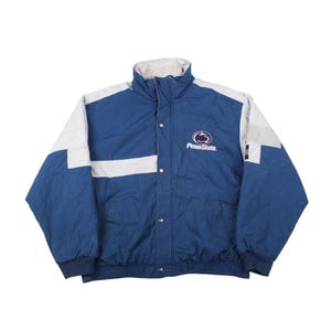 Puede incluir: Chaqueta acolchada azul y blanca con cuello alto y cierres a presión. La chaqueta presenta una franja blanca en el pecho y el logotipo de Penn State. Las mangas son azules y blancas.