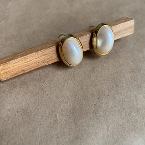 Puede incluir: Un par de pendientes ovalados de oro con piedras blancas nacaradas.