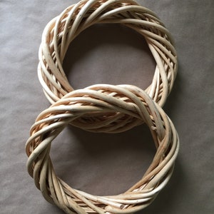 May include: Two woven wreaths made of natural wicker, arranged in the shape of the number eight. The wreaths are light brown in color and have a rustic, natural look.