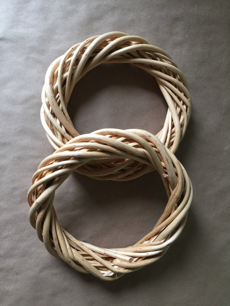 May include: Two woven wreaths made of natural wicker, arranged in the shape of the number eight. The wreaths are light brown in color and have a rustic, natural look.