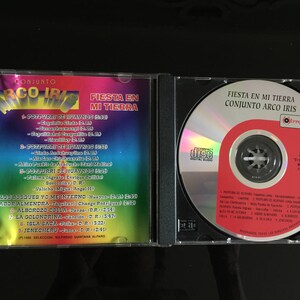 Puede incluir: Una caja de CD con un dise&ntilde;o de arco&iacute;ris y el t&iacute;tulo "Fiesta en mi tierra" de Conjunto Arco Iris. La caja de CD incluye una lista de canciones del &aacute;lbum, incluyendo "A los bosques yo me interno", "Sabor almendra", "Calborozo colla", "La golondrina", "Isla saca" y "Jenecheru".