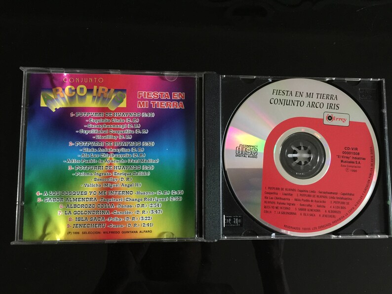 Puede incluir: Una caja de CD con un dise&ntilde;o de arco&iacute;ris y el t&iacute;tulo "Fiesta en mi tierra" de Conjunto Arco Iris. La caja de CD incluye una lista de canciones del &aacute;lbum, incluyendo "A los bosques yo me interno", "Sabor almendra", "Calborozo colla", "La golondrina", "Isla saca" y "Jenecheru".