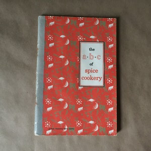 May include: A red and white book with a title that reads "the a.b.c of spice cookery". The cover has a pattern of white stars and crescent moons on a red background.