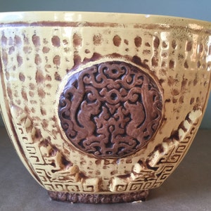 Peut inclure: Un pot en céramique jaune avec un motif en relief brun représentant un dragon et un motif géométrique autour du bord.