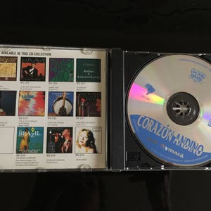 May include: A CD case with a blue and white CD inside. The CD case has a list of other CDs available in the collection. The CD is titled "Corazon Andino" with the text "Aymara" below it.