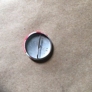 May include: The reverse of a round button featuring a red, white and blue design. The button has a metal pin on the back.