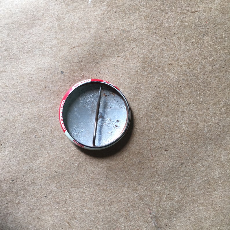 May include: The reverse of a round button featuring a red, white and blue design. The button has a metal pin on the back.