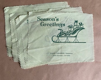 May include: Several light green cloths with a decorative edge. Each cloth features the green text "Season's Greetings" and a green illustration of a sleigh with presents. The text "STANLEY LIVINGSTON, Optometrist" is also printed.