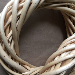 May include: A natural woven wreath made of light brown twigs, perfect for decorating a door or wall.