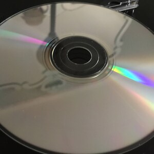 May include: A silver compact disc with a rainbow iridescent sheen. The disc has a central hole and a silver ring around the outer edge.