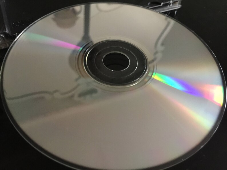 May include: A silver compact disc with a rainbow iridescent sheen. The disc has a central hole and a silver ring around the outer edge.