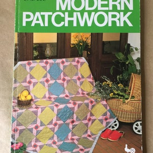 May include: A book titled "Modern Patchwork" by Ondor! featuring a colorful patchwork quilt on a tiled floor with a wicker basket and flowers.
