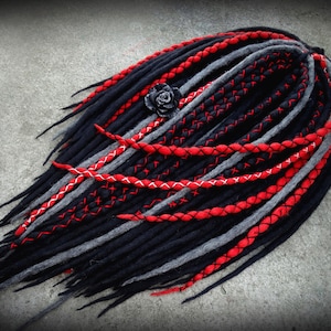 Puede incluir: Dreadlocks sintéticas negras, rojas y grises con un acento de flor negra. Las dreadlocks están trenzadas y cosidas juntas.