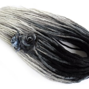 May include: A set of ombre synthetic dreadlocks with a gradient from light grey to black. The dreadlocks are arranged in a circle and have a black elastic band at the end. Two black fabric roses are attached to the dreadlocks.