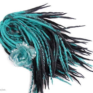 Puede incluir: Dreadlocks de lana azul turquesa y negro con un acento de flor plateada. Las dreadlocks son largas y fluidas, y la flor es un toque delicado.