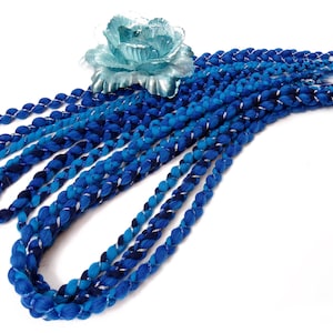 Puede incluir: Un conjunto de rastas sintéticas ombre azul y plata. Las rastas están trenzadas y tienen un hilo plateado tejido a través de ellas.