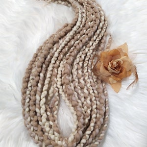 Puede incluir: Un paquete de hilo marrón y blanco con hilo dorado tejido a lo largo. El hilo está dispuesto en un círculo suelto sobre una superficie blanca y esponjosa.