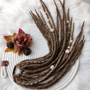 May include: A set of brown wool dreadlocks with white stitching and wooden beads. The dreadlocks are tied together with a black elastic band.