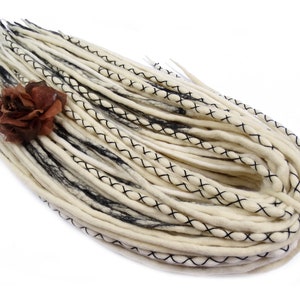 Puede incluir: Un conjunto de rastas de lana blanca con costuras negras y un acento de flor marrón.