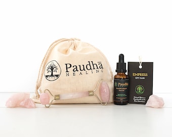 May include: A pink rose quartz facial roller, a bottle of face oil, and two rose quartz stones in a natural canvas bag. The bag has the text "Paudha Healing" printed on it. The bottle of face oil has the text "Paudha Healing" and "Nourish & Repair Face Oil" printed on it. The label on the bag has the text "Empress Gift Pack" printed on it.