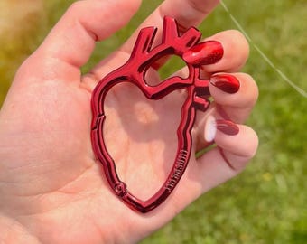 May include: A red heart-shaped keychain with a metallic finish. The keychain is held in a hand with red nail polish. The keychain has the text "Librarian" printed on it.