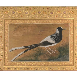 May include: A black and white bird with a long tail stands on two rocks. The bird is surrounded by a gold frame with a floral pattern. The background is a light brown color.
