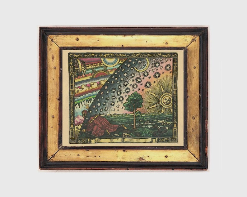 May include: A framed vintage print with a celestial theme. The artwork features a detailed illustration of the sun, moon, stars, and a figure in a red robe. The frame is a combination of dark brown and gold tones, adding to the antique aesthetic.