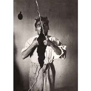 May include: A black and white photograph of a man standing in front of a cracked wall. The crack in the wall runs down the center of the man's body, creating the illusion that he is being split in two.