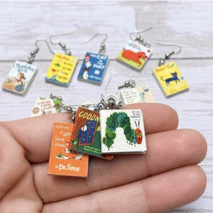 May include: A collection of miniature book earrings featuring iconic children's literature covers including The Very Hungry Caterpillar, Goodnight Moon, Green Eggs and Ham, The Cat in the Hat, Charlotte's Web, and Pete the Cat with silver hooks.