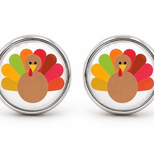 May include: A pair of round silver cufflinks featuring a graphic illustration of a brown turkey with a colorful fan-shaped tail in shades of yellow, green, orange, red, and dark red against a white background, enclosed in a polished metal frame.