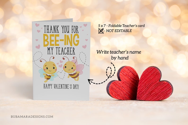 May include: A folded greeting card with the text "THANK YOU FOR BEE-ING MY TEACHER" and "HAPPY VALENTINE'S DAY!". The card features cartoon bees and hearts. Two red wooden hearts are next to the card.