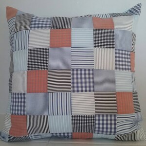 May include: Square patchwork pillow with a variety of patterns, including stripes, checks, and solid colors in shades of blue, white, and coral. The pillow has a square shape with a corner detail.