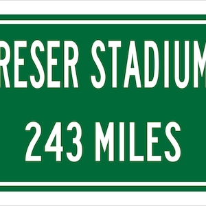 May include: Green road sign with white text that reads "Reser Stadium 243 Miles".