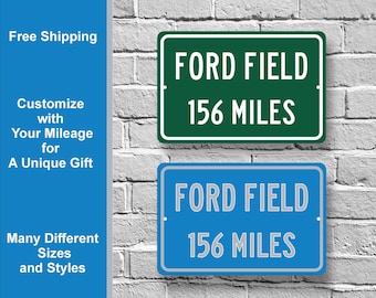 Puede incluir: Dos letreros de metal con fondo blanco y texto negro. El letrero superior es verde con el texto "FORD FIELD 156 MILES". El letrero inferior es azul con el mismo texto.