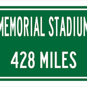 May include: Green road sign with white lettering that reads "Memorial Stadium 428 Miles".