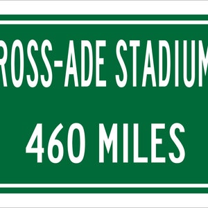 May include: A green road sign with white lettering that reads "ROSS-ADE STADIUM 460 MILES".