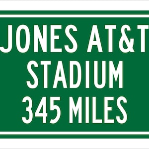 May include: Green road sign with white text that reads "Jones AT&T Stadium 345 Miles".