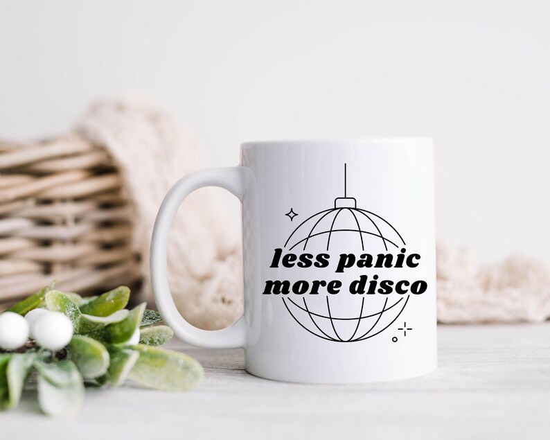 May include: White ceramic coffee mug with a black outline of a disco ball and the text "less panic more disco".