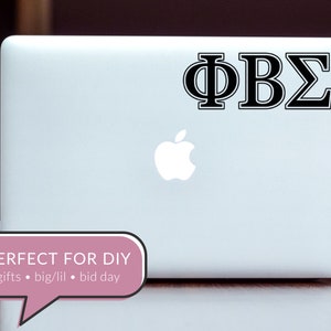 May include: A white laptop computer with a black Apple logo and a black vinyl sticker with the Greek letters "&Phi;&Beta;&Sigma;" on the lid. The laptop is sitting on a wooden surface.
