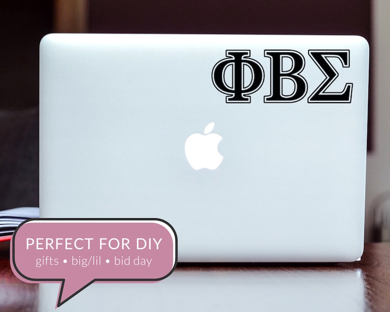 May include: A white laptop computer with a black Apple logo and a black vinyl sticker with the Greek letters "&Phi;&Beta;&Sigma;" on the lid. The laptop is sitting on a wooden surface.