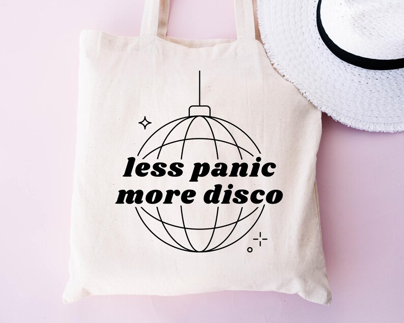 May include: A white tote bag with black text that reads "less panic more disco" and a black line drawing of a disco ball.
