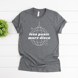 May include: A dark gray t-shirt with a white disco ball graphic and the text "less panic more disco".