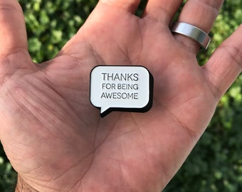 May include: White enamel pin with black outline in the shape of a speech bubble. The pin says "Thanks for being awesome".