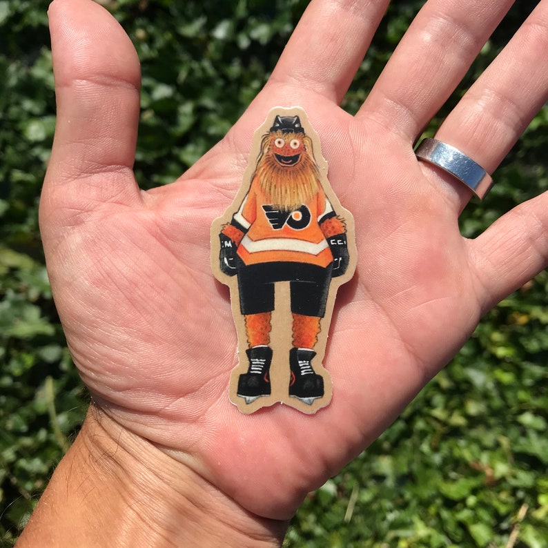 May include: A brown and orange hockey player sticker with a furry face and the letter "O" on the jersey.