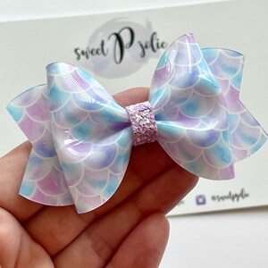May include: A light blue and purple mermaid scale hair bow with a sparkly pink center.