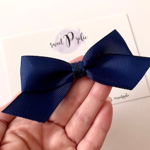 May include: A navy blue bow with a glittery center. The bow is made of a ribbed fabric and is displayed on a white card with the text "sweet P jolie" and the @sweetpjolie social media handle.
